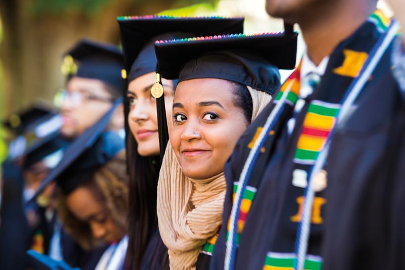 A close up of an Emory graduate--isolated by the camera's focus amid a line other graduates--smiles broadly.