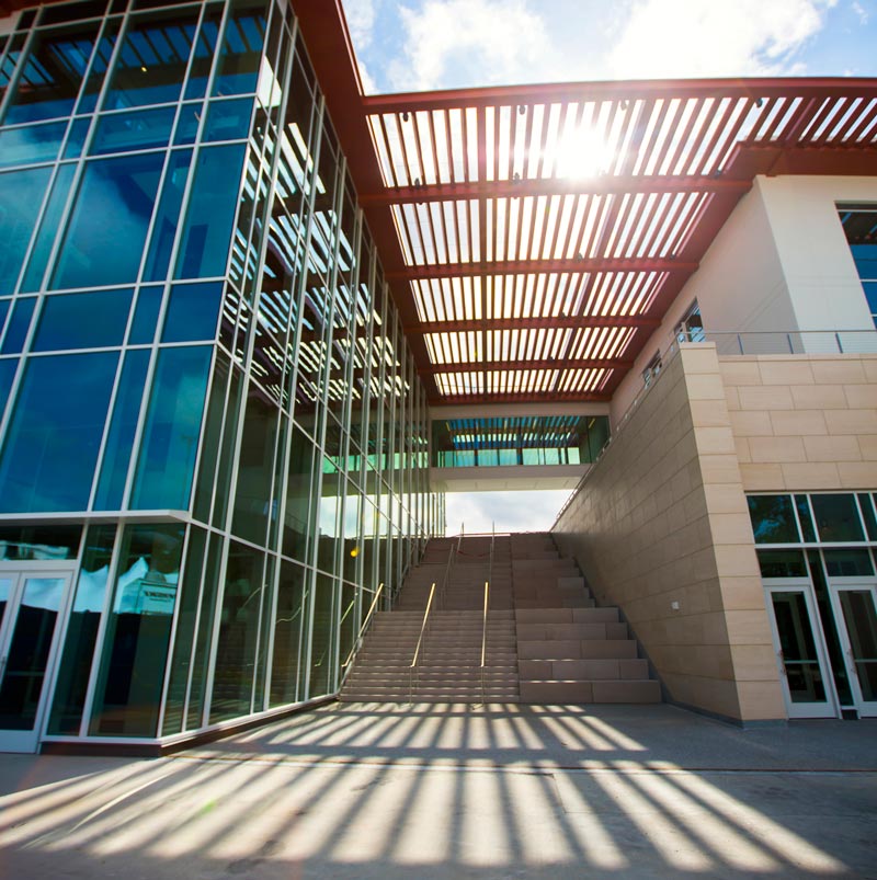 The front steps of the new Student Center, with sunlight shining through latticework, casting shadows with strong vanishing perspective in the foreground.