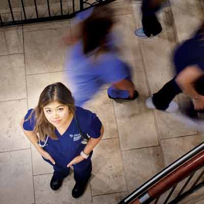 A nursing student standing on a staircase as other hospital workers walk past.