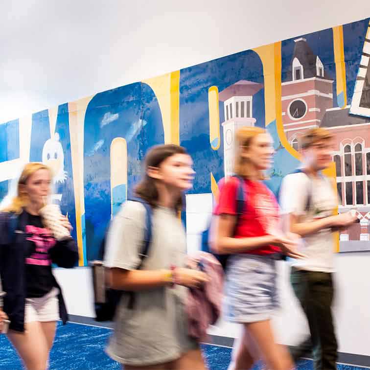 Students walking in front of an Emory text mural