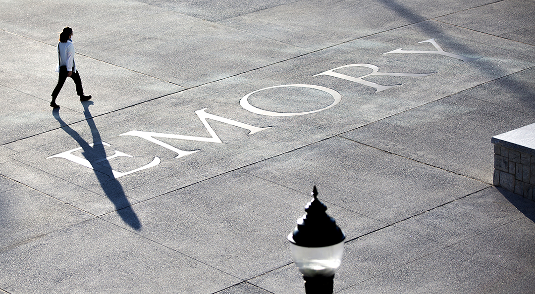 woman walking across pavement with the word Emory embedded in the concrete